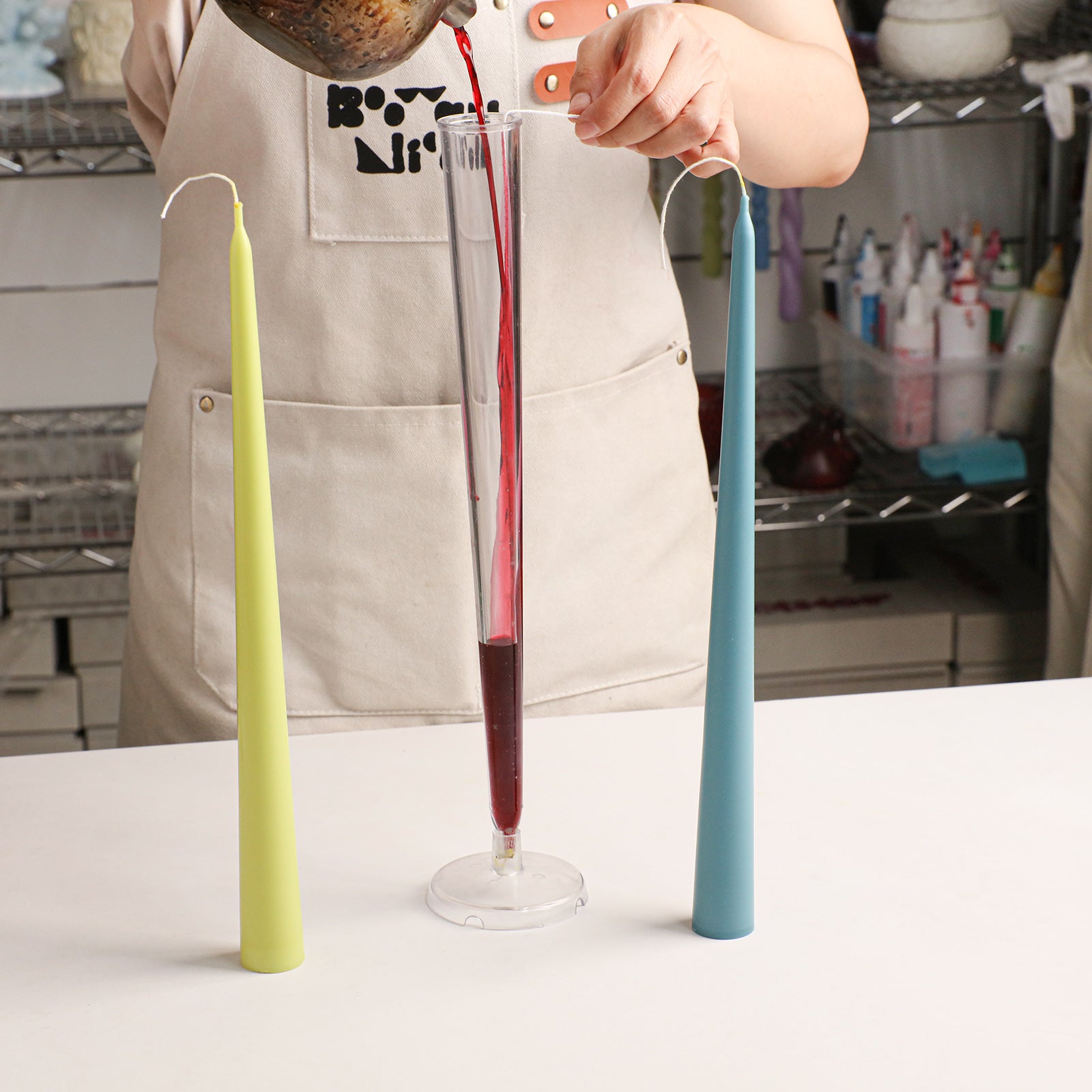Smooth Taper Acrylic Candle Mold, pouring melted wax into clear mold with finished taper candles - Boowan Nicole