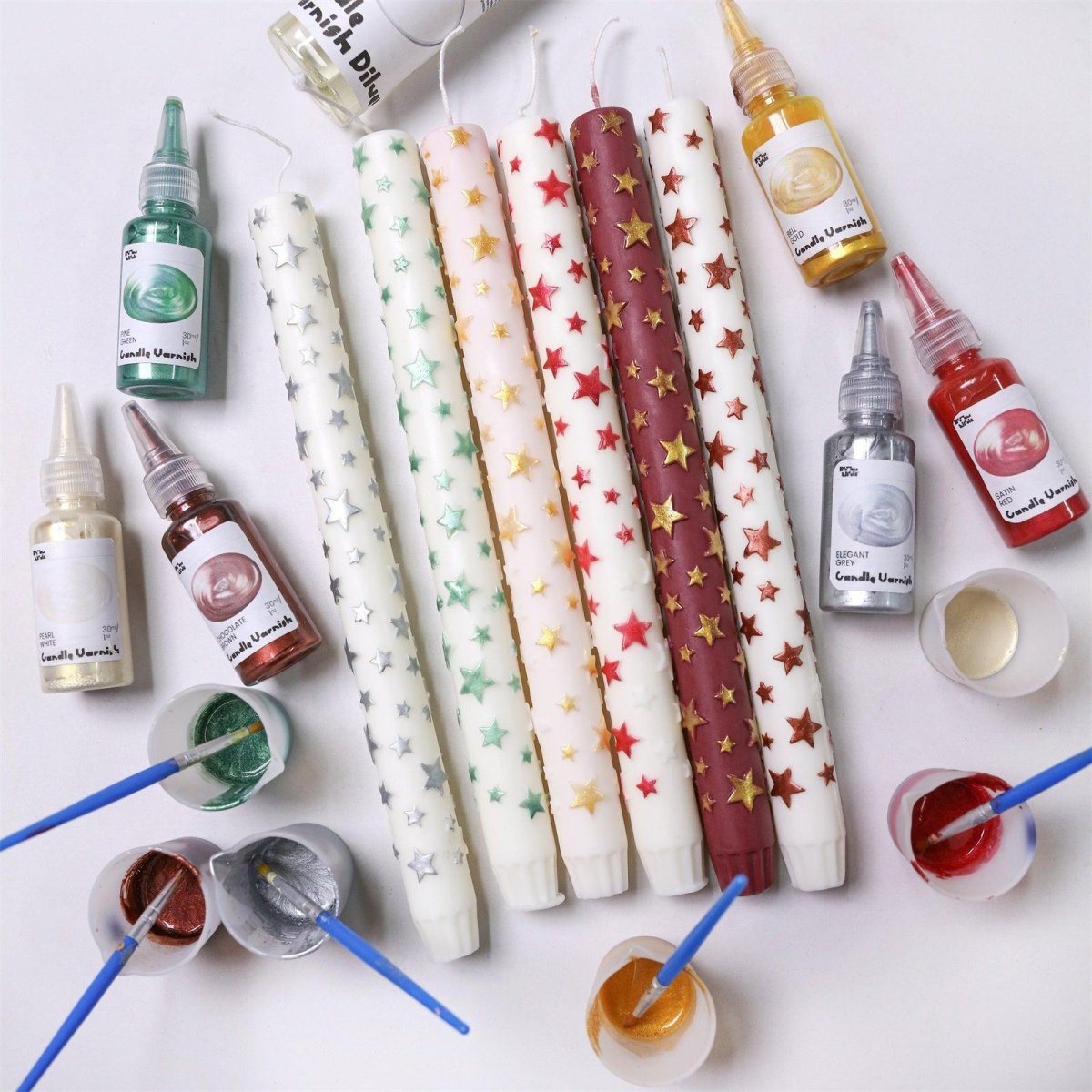 Hand-painted taper candles with raised stars in red, gold, green, and silver, displayed with matching varnish paints and brushes for DIY decoration - Boowan Nicole