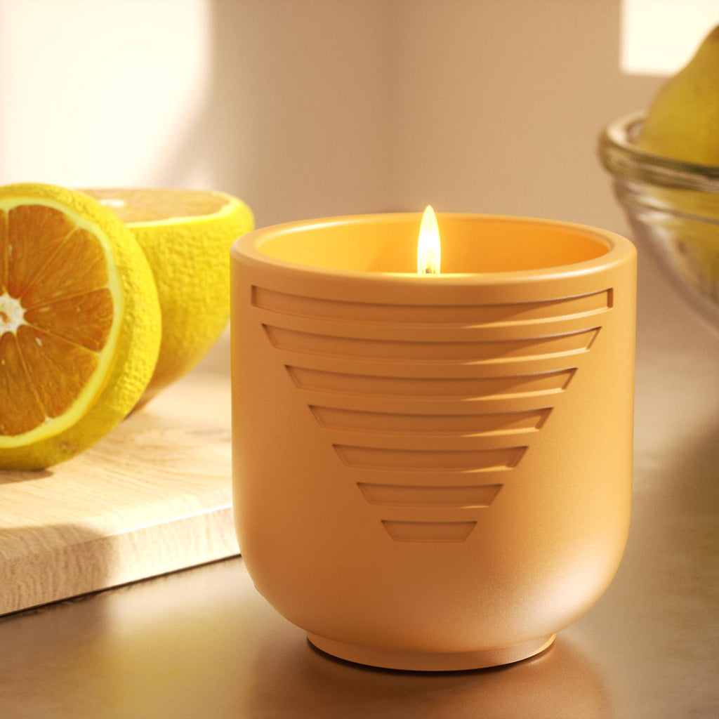 Lit candle in orange geometric jar with sliced oranges on counter - Boowan Nicole
