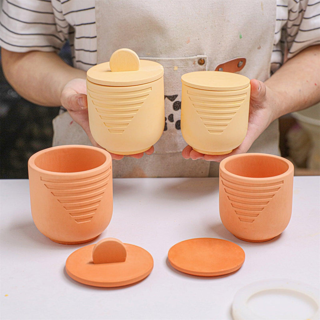 Hands holding a large geometric candle jar with flat lid and a small jar with raised lid - Boowan Nicole