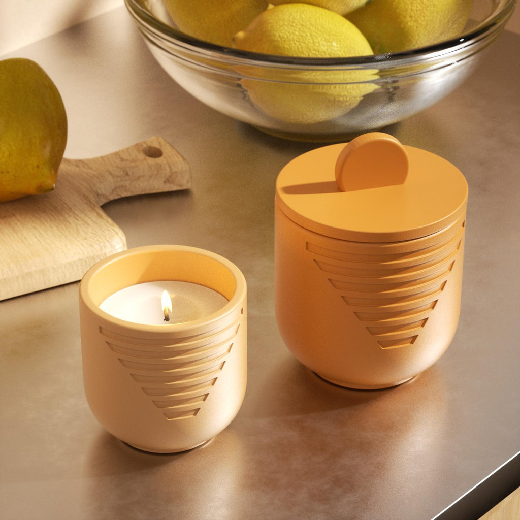 Lit candle and lidded orange jar on kitchen counter with lemons - Boowan Nicole