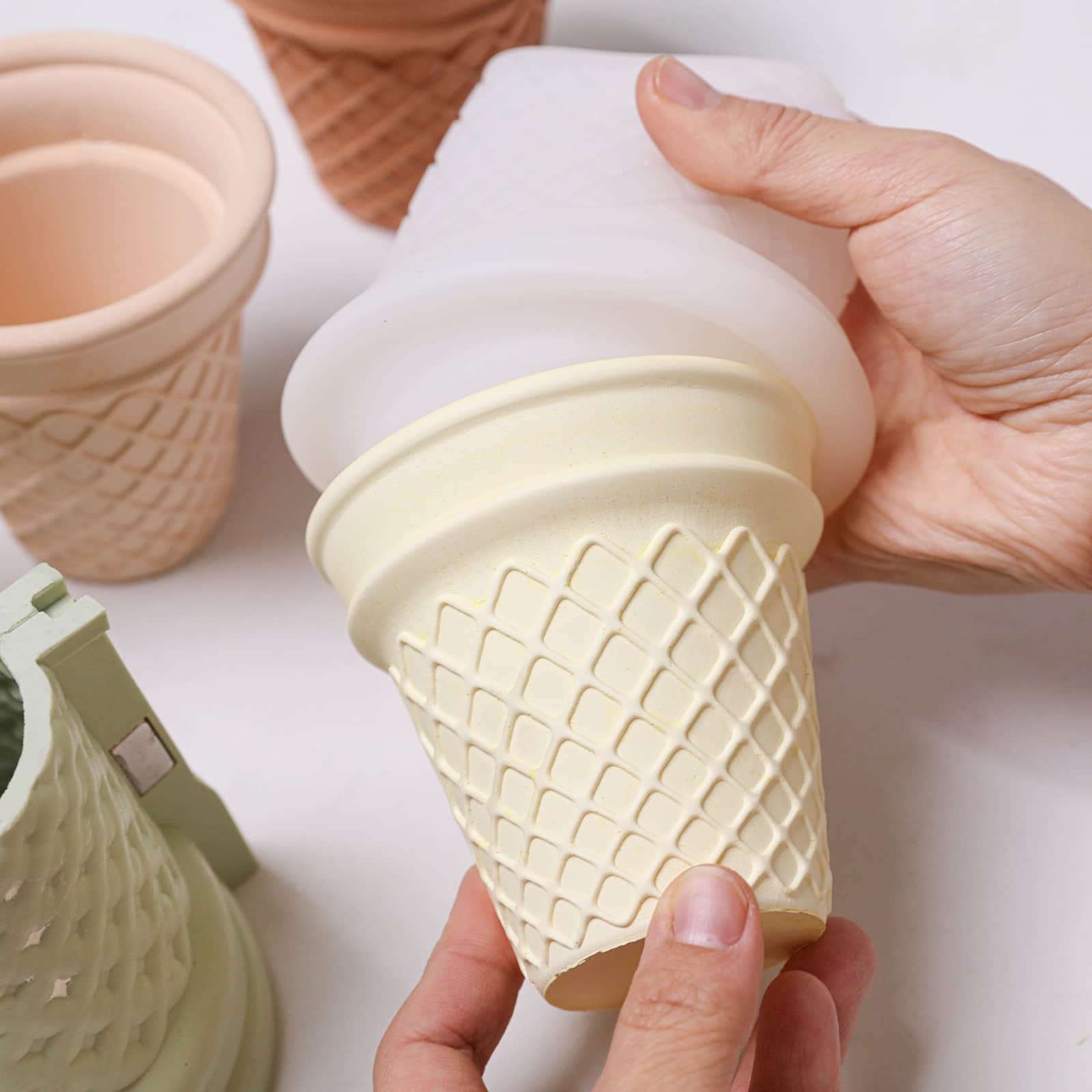 Hands unmolding an ice cream cone–style candle jar from the Sweet Swirl Sundae silicone mold, with waffle texture and support shell visible - Boowan Nicole