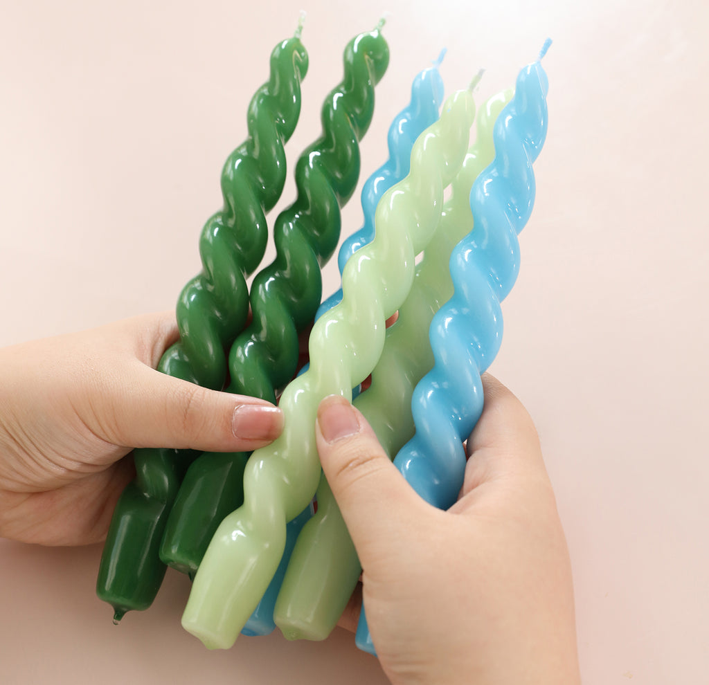 Holding a hand-held display of six tapered spiral candles with smooth surfaces in blue, green and cyan, -Boowan Nicole