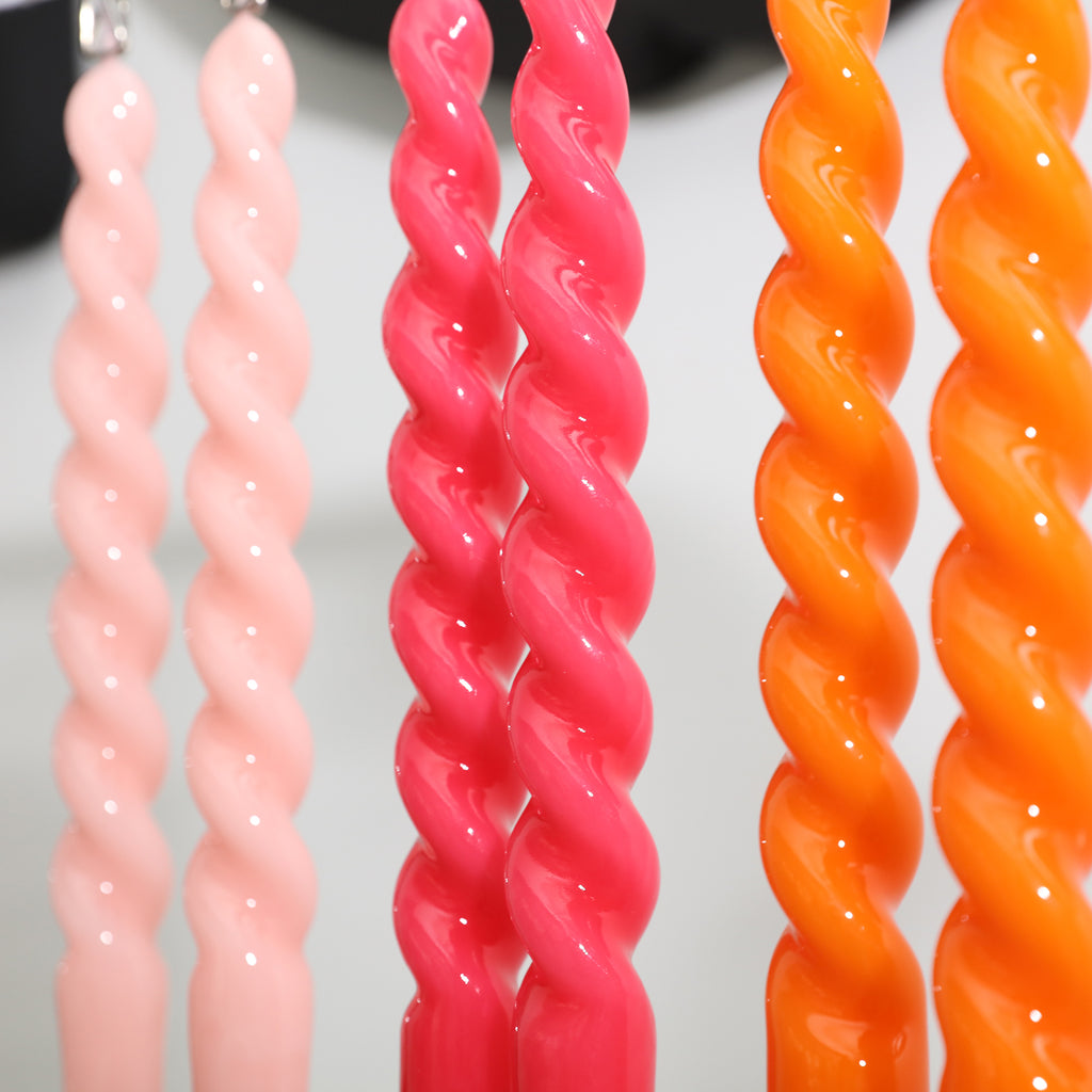 Six tapered spiral candles in orange, red and pink placed on a rack to dry - Boowan Nicole