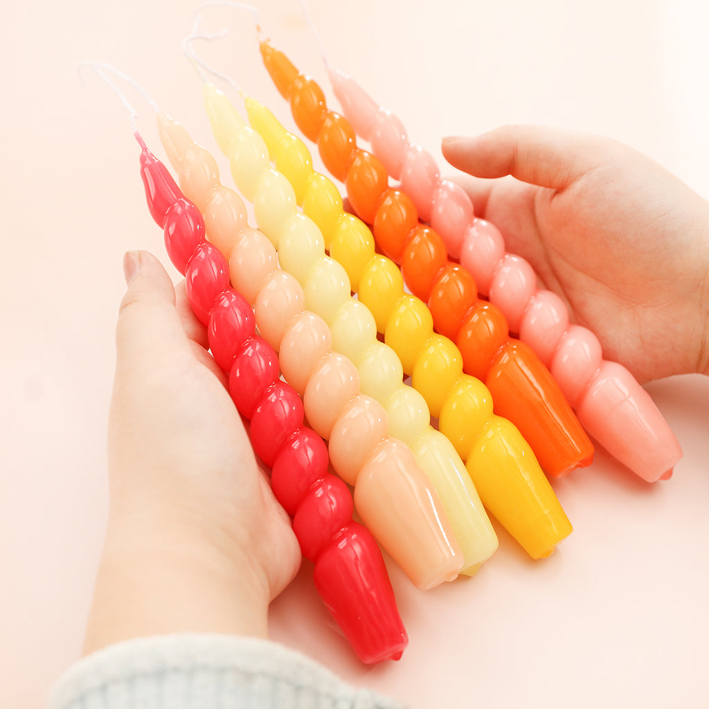 Displaying six tapered spiral candles in gradient colors of pink, yellow and red in hand - Boowan Nicole