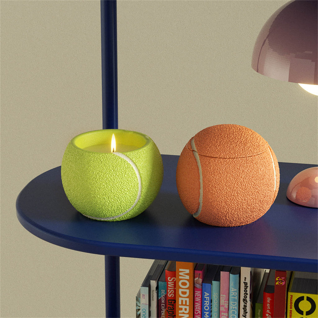 Tennis ball–shaped candle jars on a blue shelf—neon yellow lit, orange with lid—pebble texture and white seams, sporty home décor - Boowan Nicole