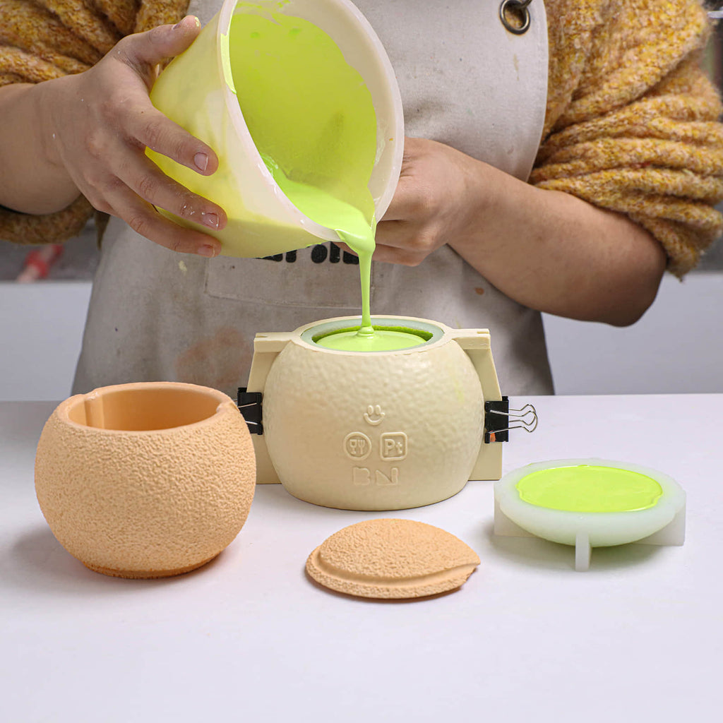 Pouring prepared pigmented concrete into a tennis-ball candle jar silicone mold with a support shell - Boowan Nicole