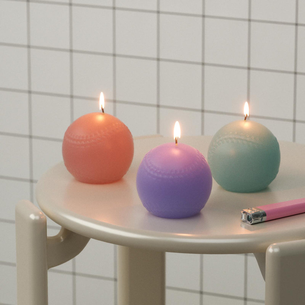 Three colorful spherical candles on a small round table with a tiled wall background.