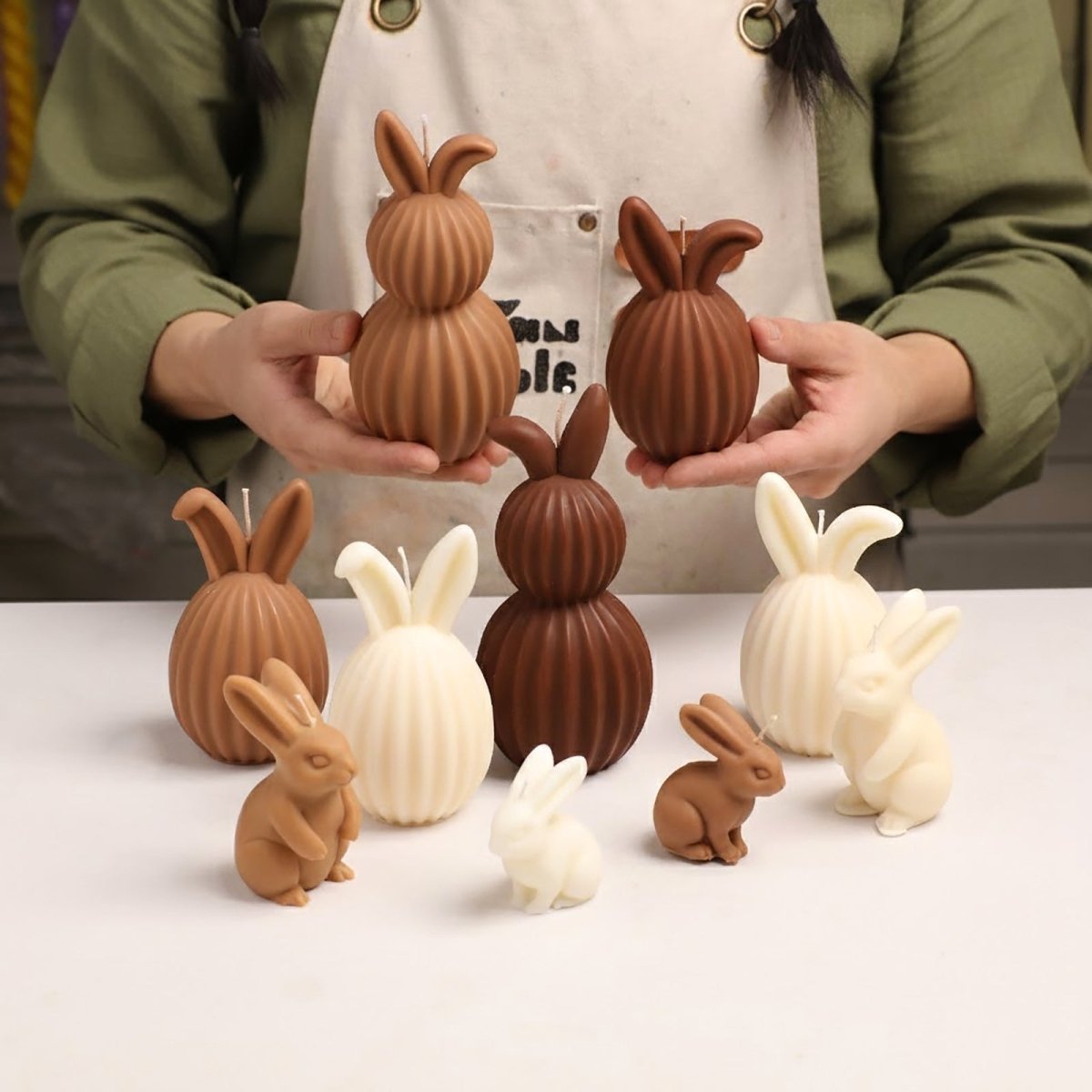 Artisan holding brown ribbed bunny candles from The Little Bunny Show silicone mold collection, surrounded by realistic rabbit designs - Boowan Nicole