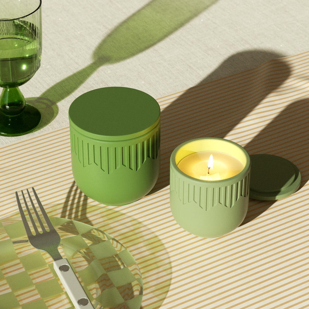 Lit green candle jar and closed jar on striped tablecloth with glass and plate - Boowan Nicole