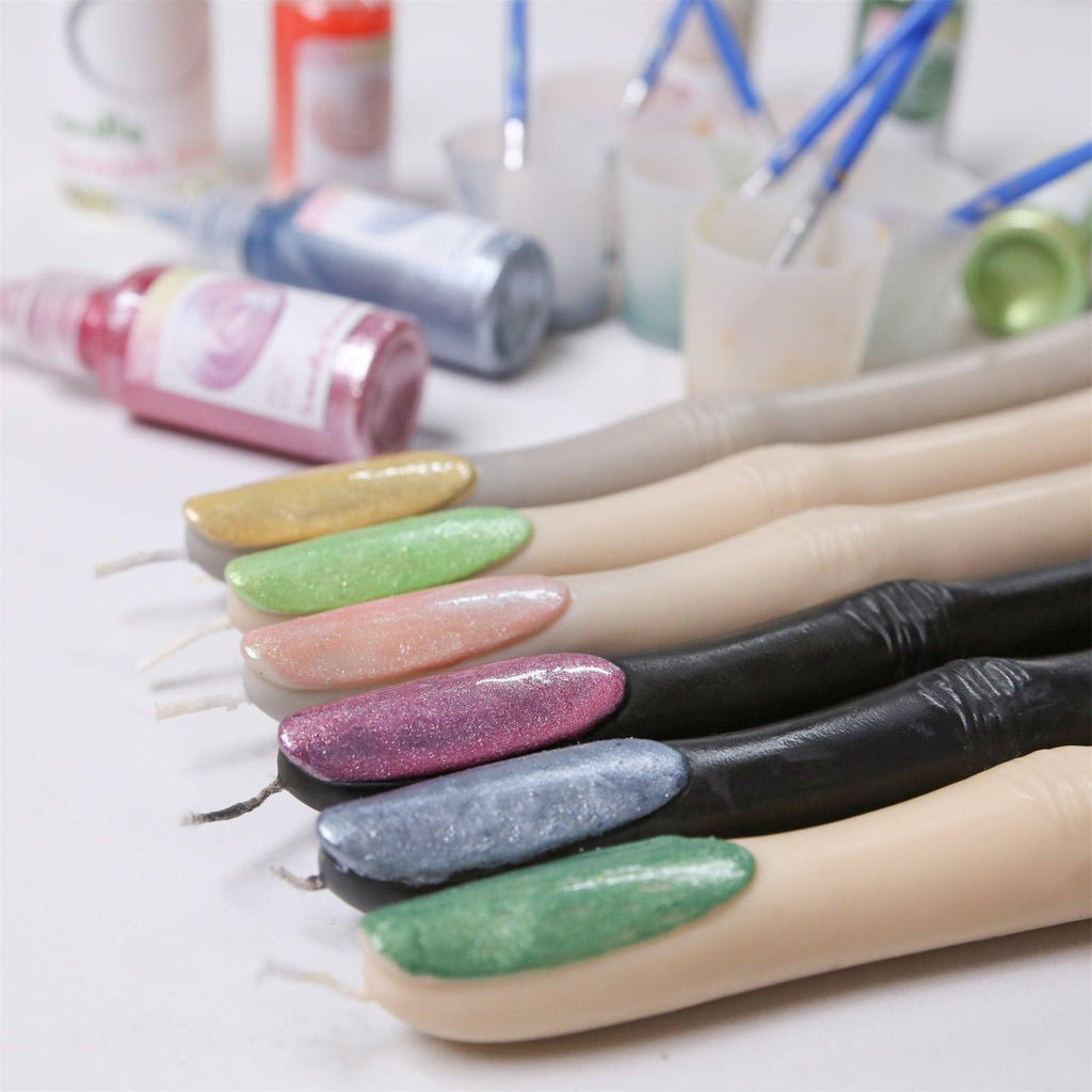 Colorful witch’s finger-shaped candles with glittery painted nails in green, pink, gold, purple, and silver, displayed with mica powders, brushes, and painting tools in the background - Boowan Nicole