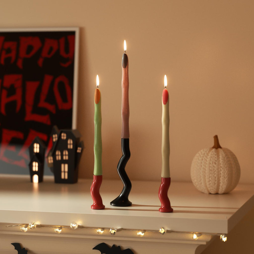 Three lit witch’s finger-shaped candles in Halloween colors displayed on a decorated mantel with festive props - Boowan Nicole