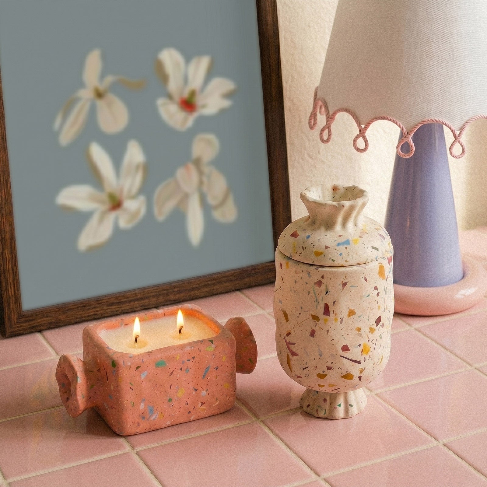 Pair of terrazzo wrapped bonbon candle jars arranged on pink tile beside vintage table lamp interior styling - Boowan Nicole