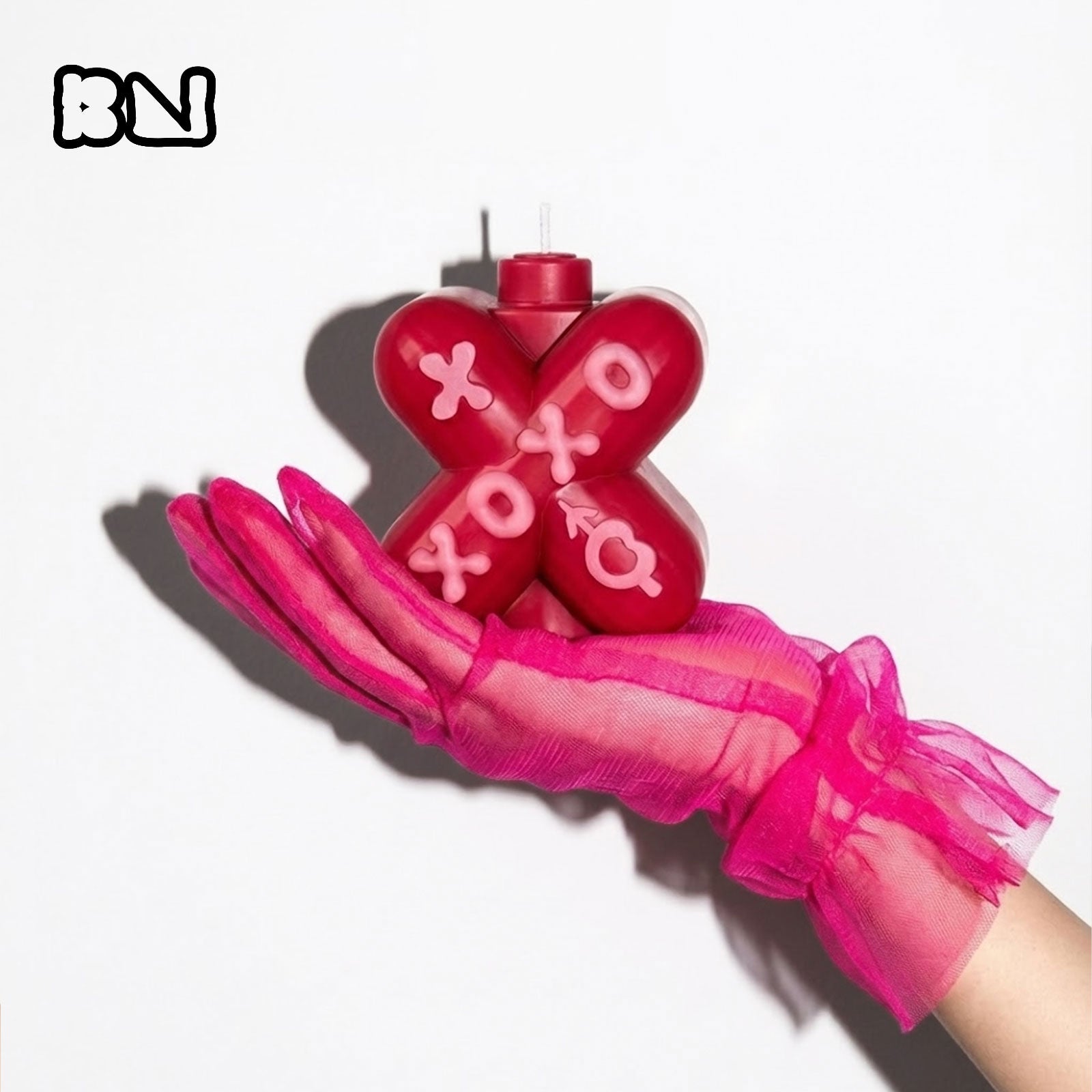 Red X-shaped XOXO candle held by a hand in a pink sheer glove - Boowan Nicole