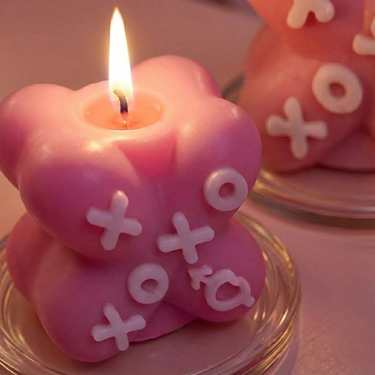 Close-up of a lit pink X-shaped XOXO candle with white embossed letters - Boowan Nicole
