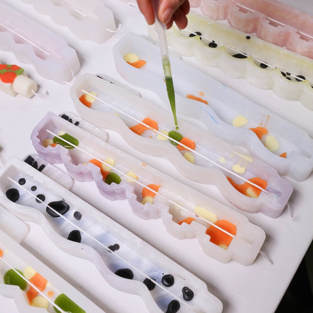 Hand using a dropper to add green wax into zigzag taper candle silicone molds with centered wicks - Boowan Nicole