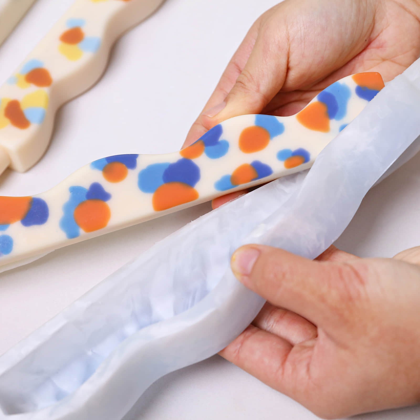 Hands unmolding a wavy zigzag taper candle with colorful confetti dots from a silicone mold - Boowan Nicole