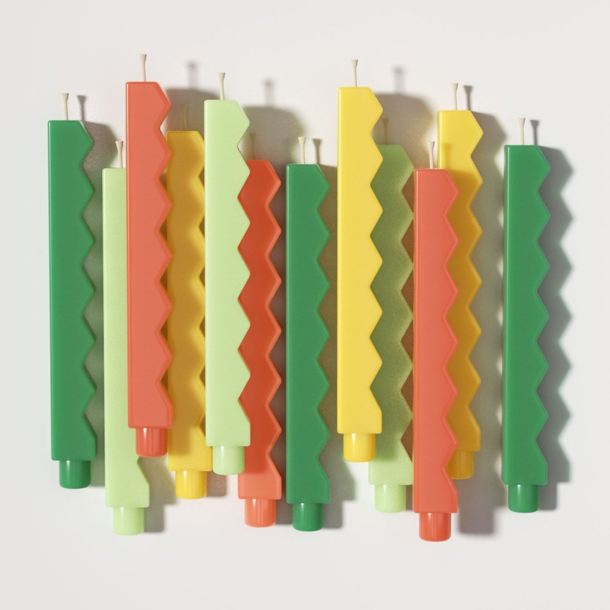 Colorful zigzag-edge taper candles flat lay in green, yellow, and orange tones - Boowan Nicole