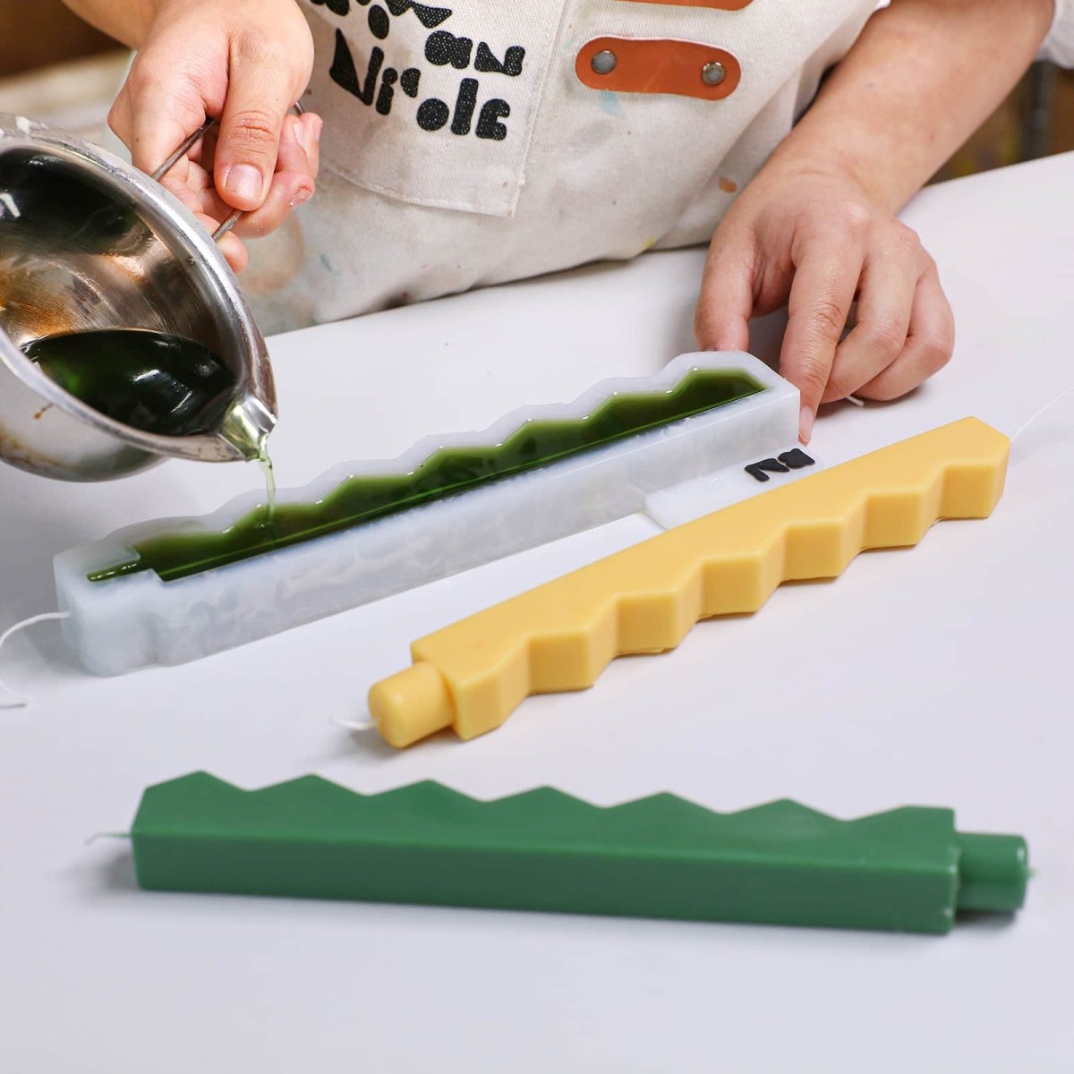 Pouring green wax into a zigzag-edge taper candle silicone mold with centered wick - Boowan Nicole