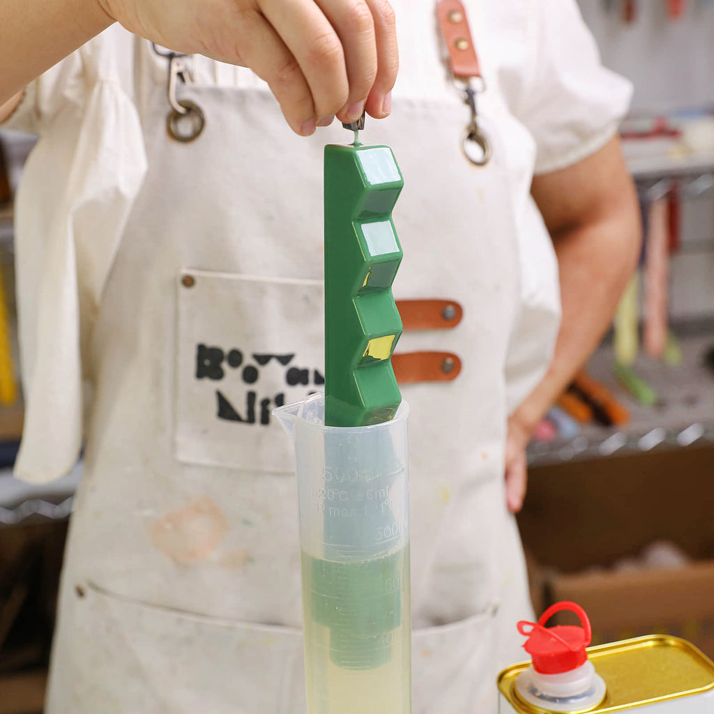 Hand dipping a green stair-step taper candle into a tall measuring beaker - Boowan Nicole