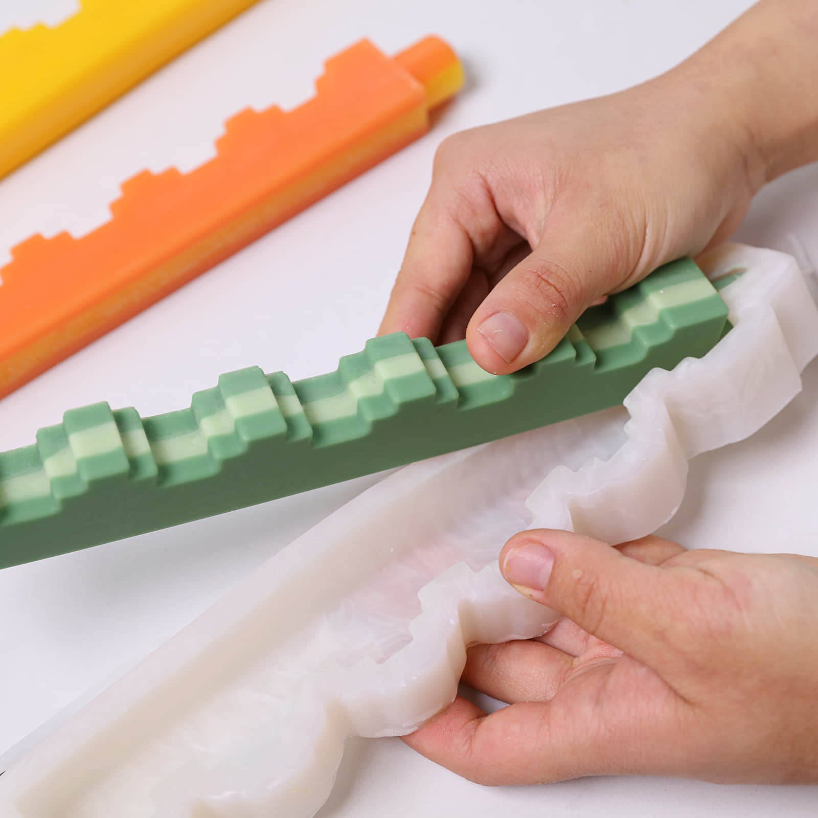 Hands demolding a green stair-step taper candle from a white silicone mold - Boowan Nicole