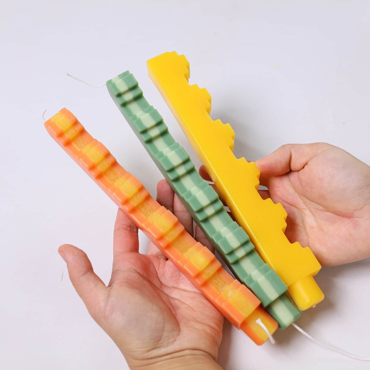 Hands holding three step-edge taper candles in yellow, green, and orange - Boowan Nicole