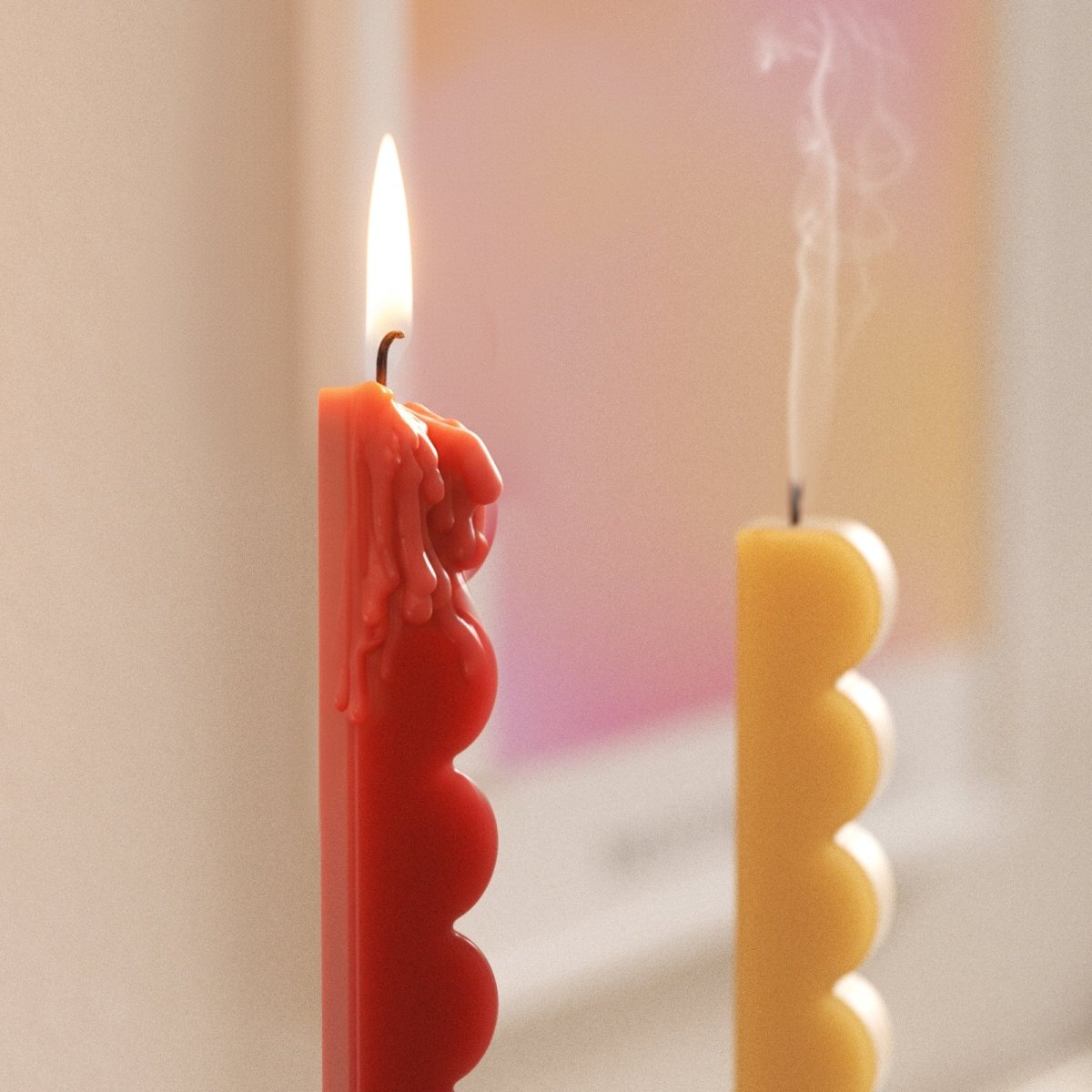 Close-up of red wavy-edge taper candle with wax drips; yellow taper extinguished with smoke in the background - Boowan Nicole