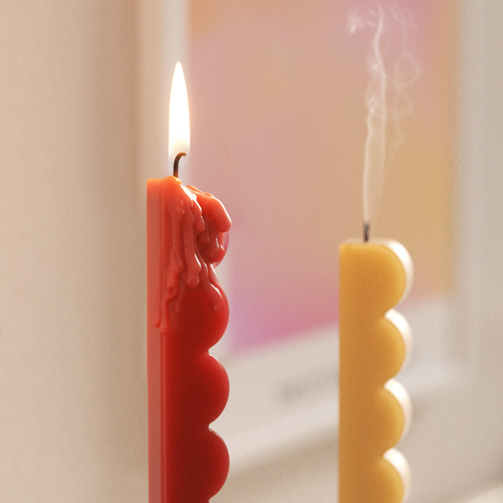 Close-up of red wavy-edge taper candle with wax drips; yellow taper extinguished with smoke in the background - Boowan Nicole
