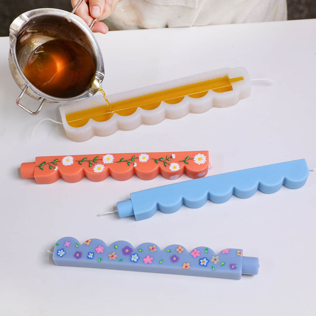 Pouring amber wax into a scalloped-edge taper candle silicone mold; finished floral and blue tapers nearby - Boowan Nicole