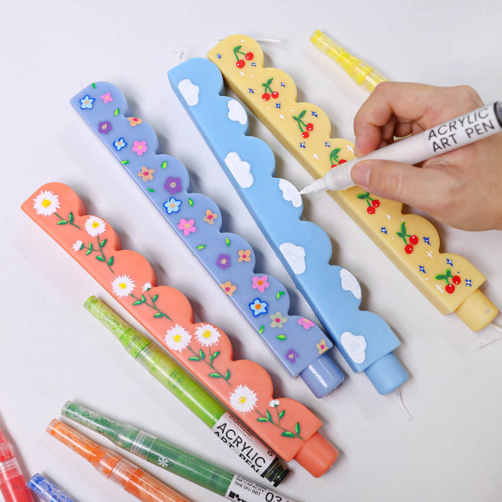 Hand painting white clouds on pastel scalloped-edge taper candles with an acrylic art pen -Boowan Nicole
