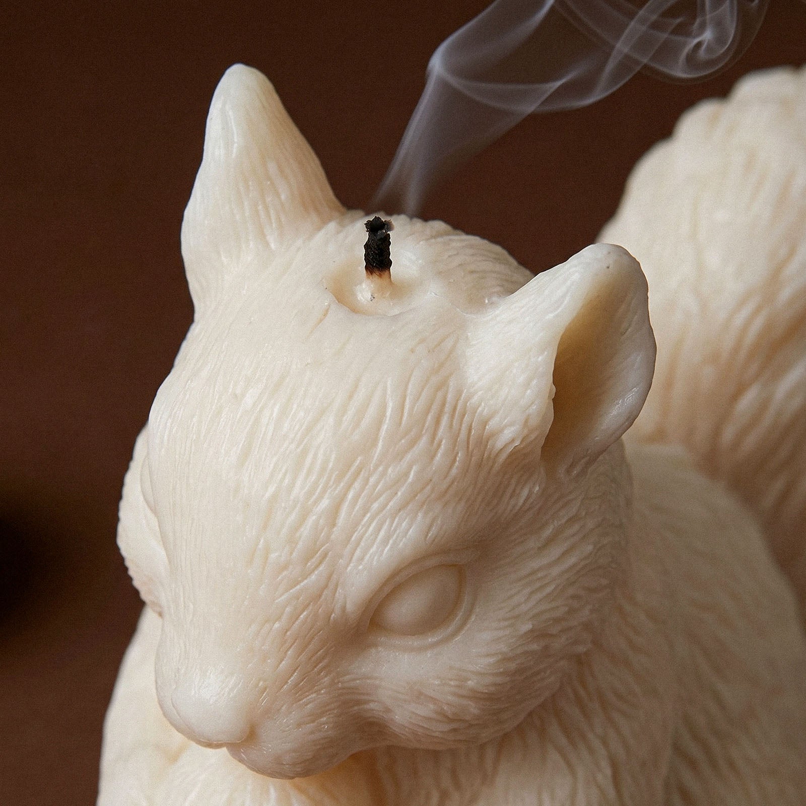 Close-up of an extinguished ivory Acorn Hug Squirrel Candle showing detailed fur texture around the ears and face, with a wisp of smoke rising from the wick.
