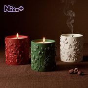 Three Berry Vine Candle Jars burning side by side in red, green, and cream, each wrapped in a berry vine relief, with blackberries scattered on a brown fabric surface and the Nico+ collaboration logo in the corner.