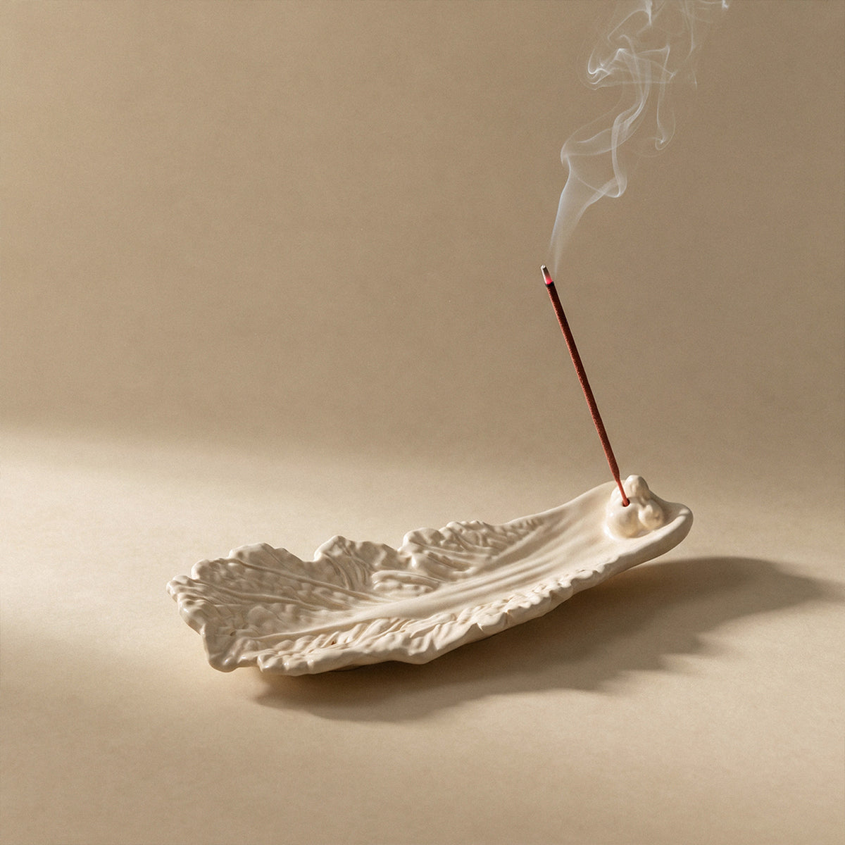 Cream-coloured cabbage leaf incense holder with a burning incense stick