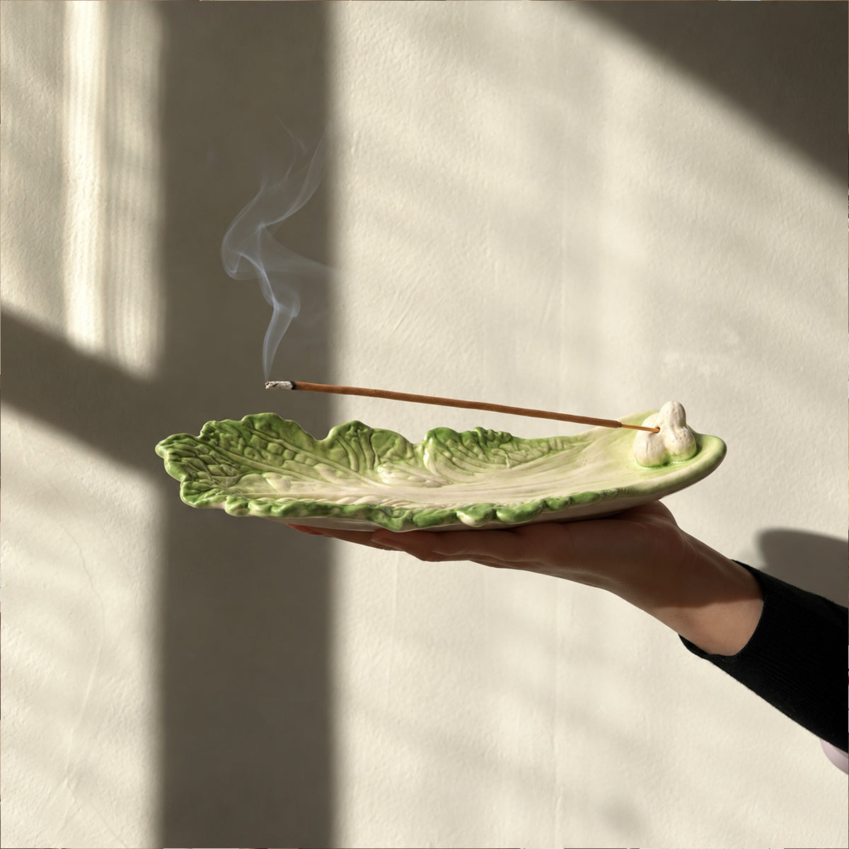 Hand holding a green cabbage leaf incense holder with incense smoke