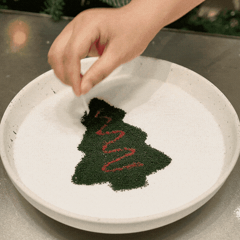 Drawing a Christmas tree design with green and red sand wax on white