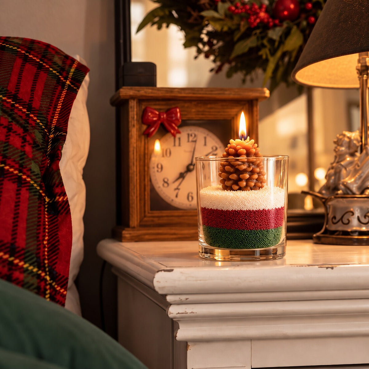 Layered red, white and green sand wax candle with pinecone on a nightstand