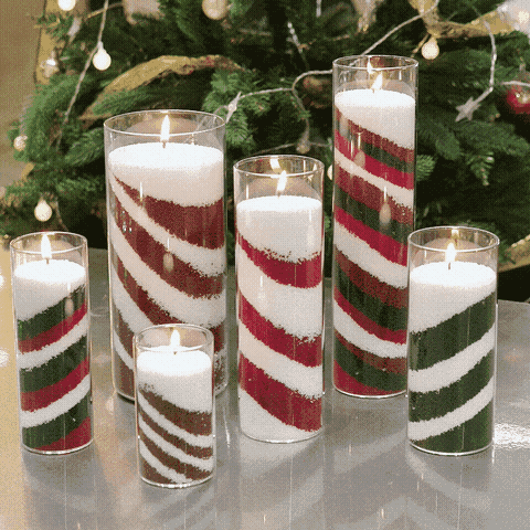 Red, green and white striped sand wax pillar candles in glass vases by a Christmas tree