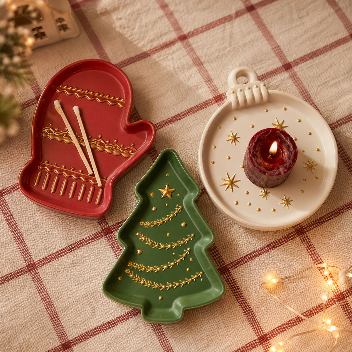 Red mitten tray, green tree tray and cream ornament tray holding a lit candle on a plaid tablecloth