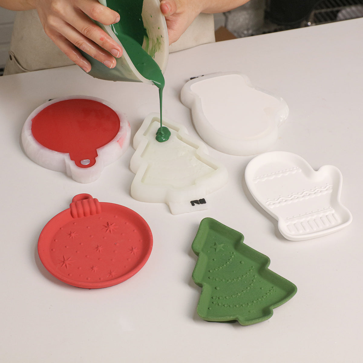 Pouring green cement into the Christmas tree tray silicone mold beside the ornament and mitten molds