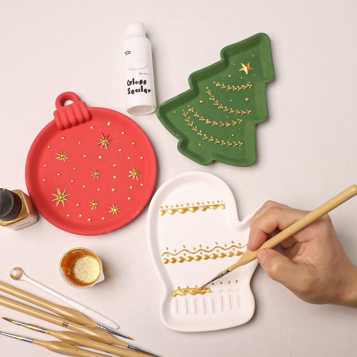 Painting gold details on a mitten tray with a fine liner brush next to gloss sealer and gold mica powder