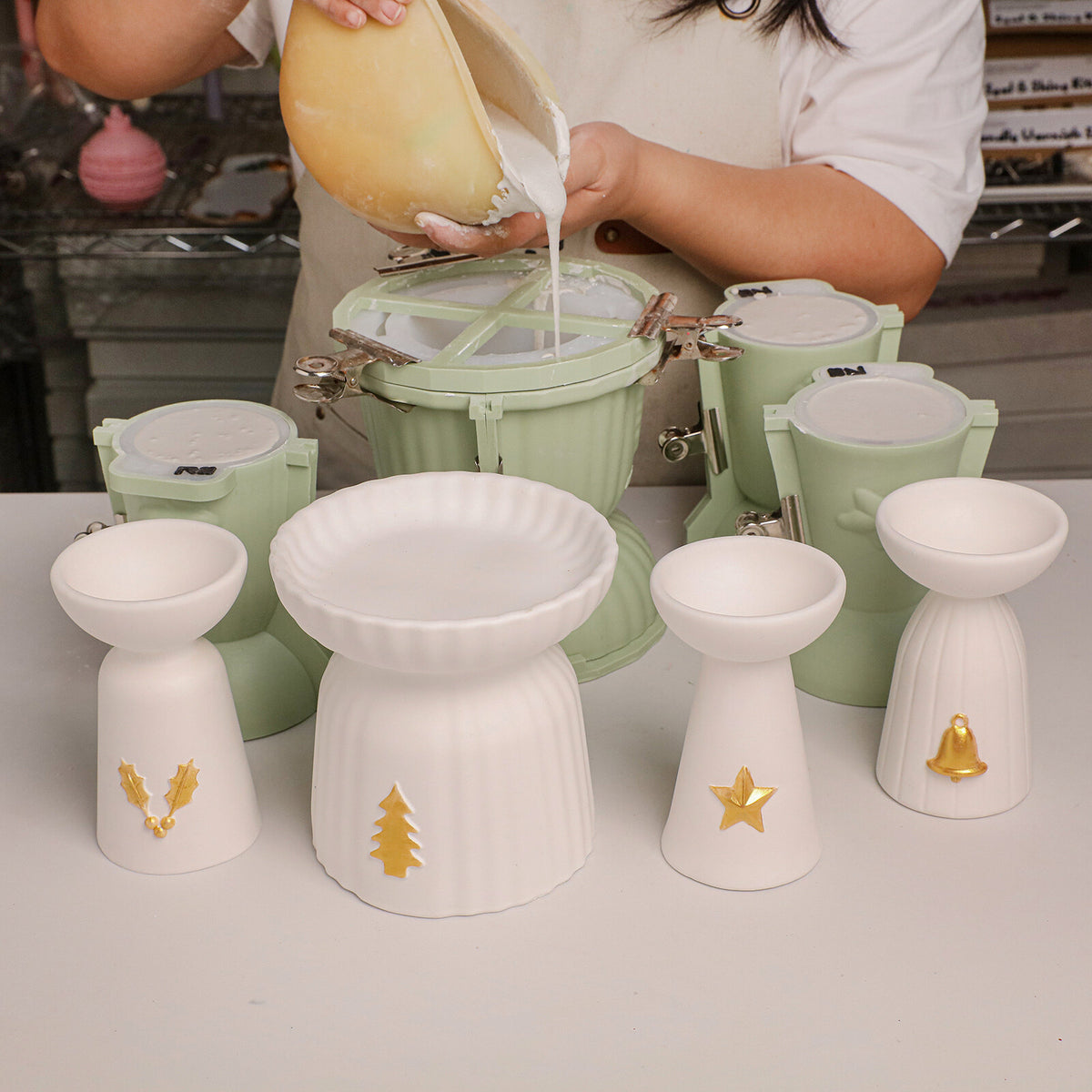 Maker pouring OmniCast cement into green silicone molds next to finished white candle holders
