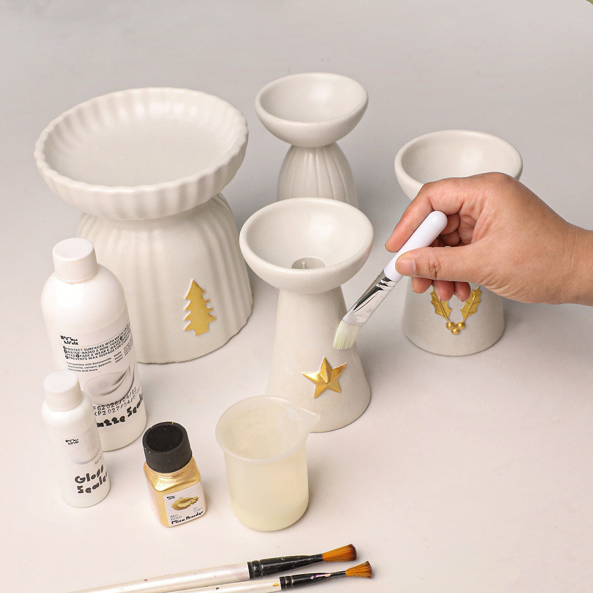 Painting the gold charms on white candle holders with sealer, mica powder and brushes