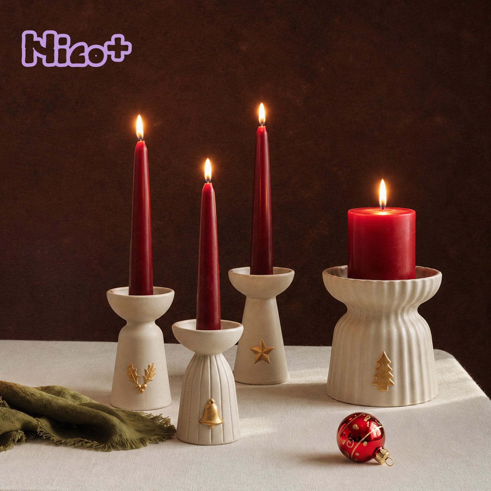 Four Azulmostaza x Boowan Nicole Christmas Glow ceramic-look candle holders — holly, bell, star, and a large ribbed tree charm pillar holder — with lit red taper and pillar candles on a linen tablecloth, Nico+ logo in the corner.