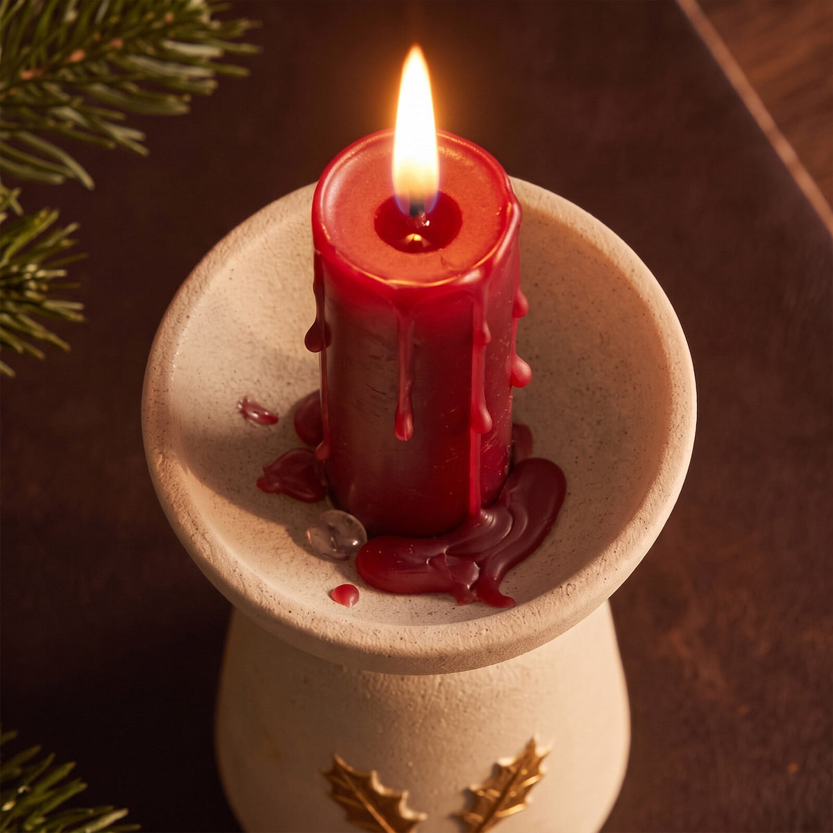 Close-up of a dripping red pillar candle in the ribbed tree charm candle holder with gold holly accents