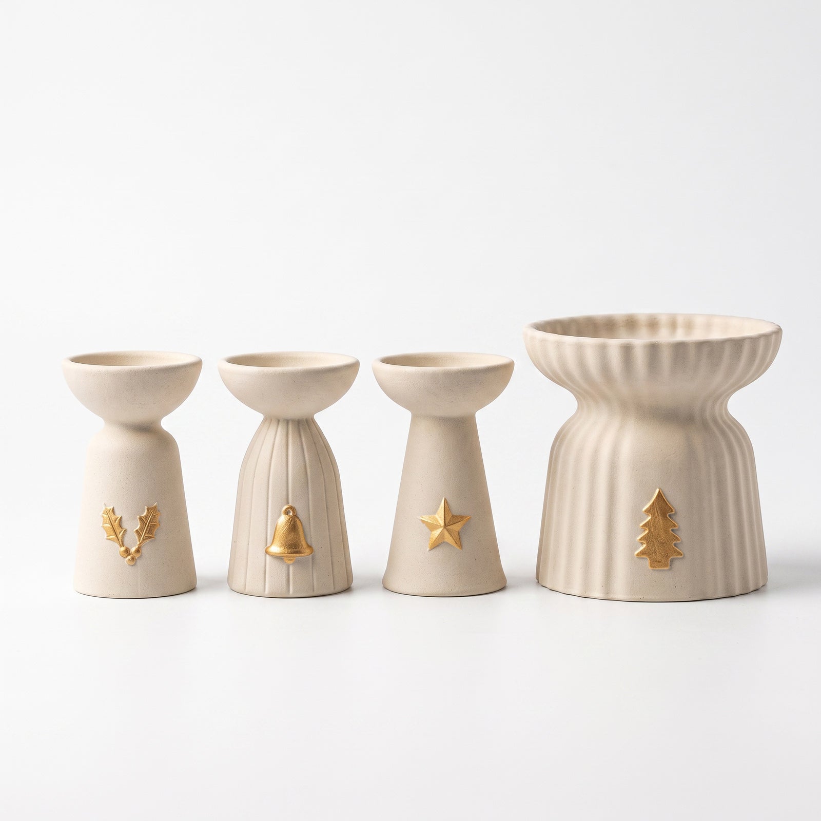 Four Christmas Glow candle holders in a row on a white background — holly, bell, and star charm taper holders beside a larger ribbed pillar holder with a gold tree charm.