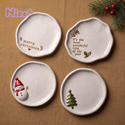 Four organic ceramic-look trinket trays with Christmas designs — snowman, Merry Christmas text, It's the Most Wonderful Time of the Year text, and Christmas tree — arranged on tan linen with a pine branch and red berries, Nico+ logo in the corner.