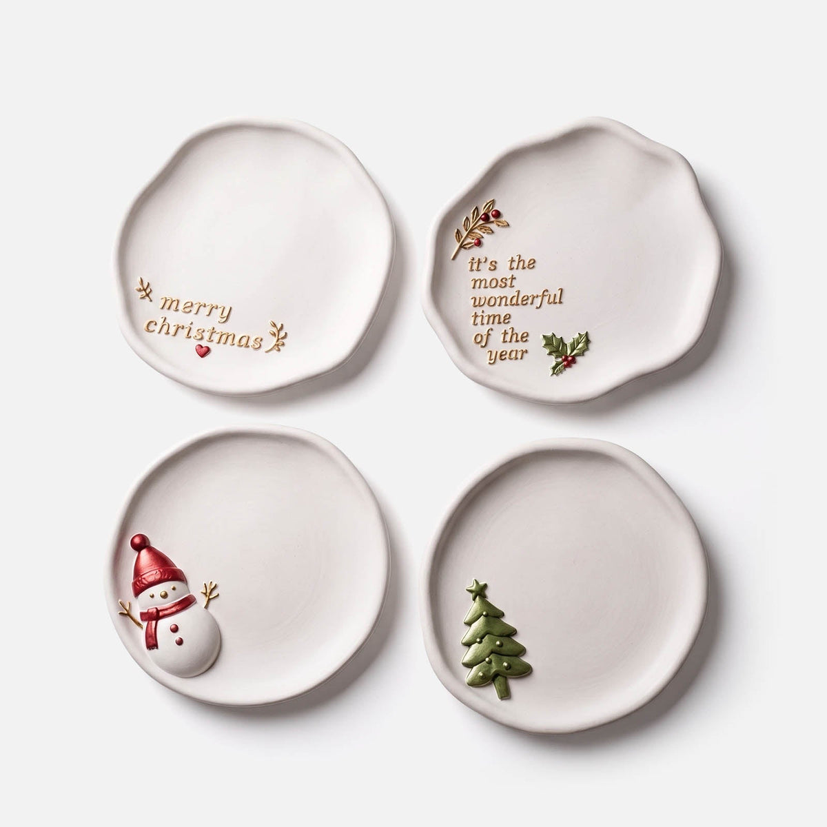 Four organic ceramic-look Christmas trinket trays — snowman, Merry Christmas text, It's the Most Wonderful Time of the Year text, and Christmas tree designs — on a white background.