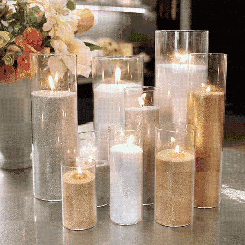 Glass pillar vases filled with gold, silver and white pearl sand wax candles burning