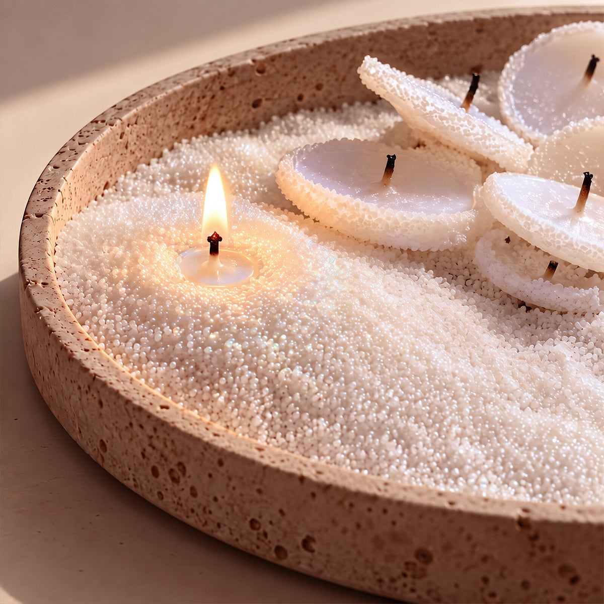Stone tray of white pearl sand wax with lit wax disc candles