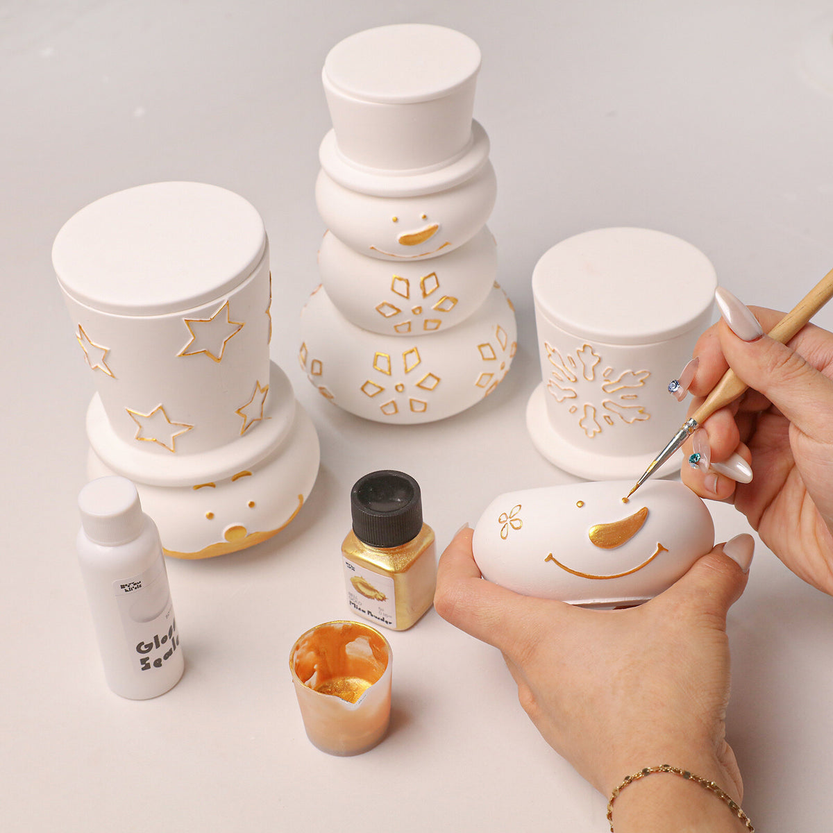Painting gold snowflakes on a snowman candle jar